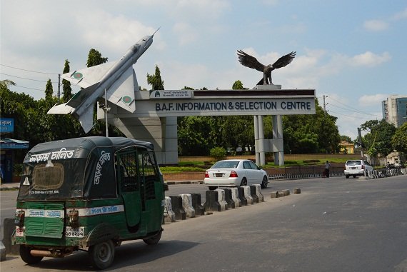 A rickshaw in front of a Bangladesh Airforce Center, with a MiG-21 mounted as a gateguard. Rickshaws use pressurized gas for propulsion.