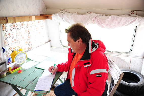Karl Helm beim Führen der Papiere im Schreibbüro, einem alten Wohnwagen Karl Helm beim Führen der Papiere im Schreibbüro, einem alten Wohnwagen