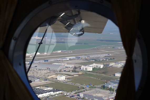 Wr Neustadt Anflug: Blick durch die liebevoll mit Vorhängen versehenen Bullaugen-Fenster auf den Flugplatz Wr. Neustadt Ost beim Eindrehen zur Piste 09.