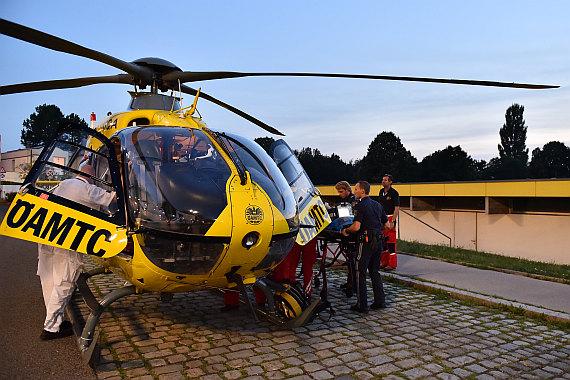 Links der Notarzt des NEF, der mit dem im Hubschrauber befindlichen Kollegen medizinische Details bespricht, während Polizisten und Sanitäter die Trage mit dem Kleinkind einladen.