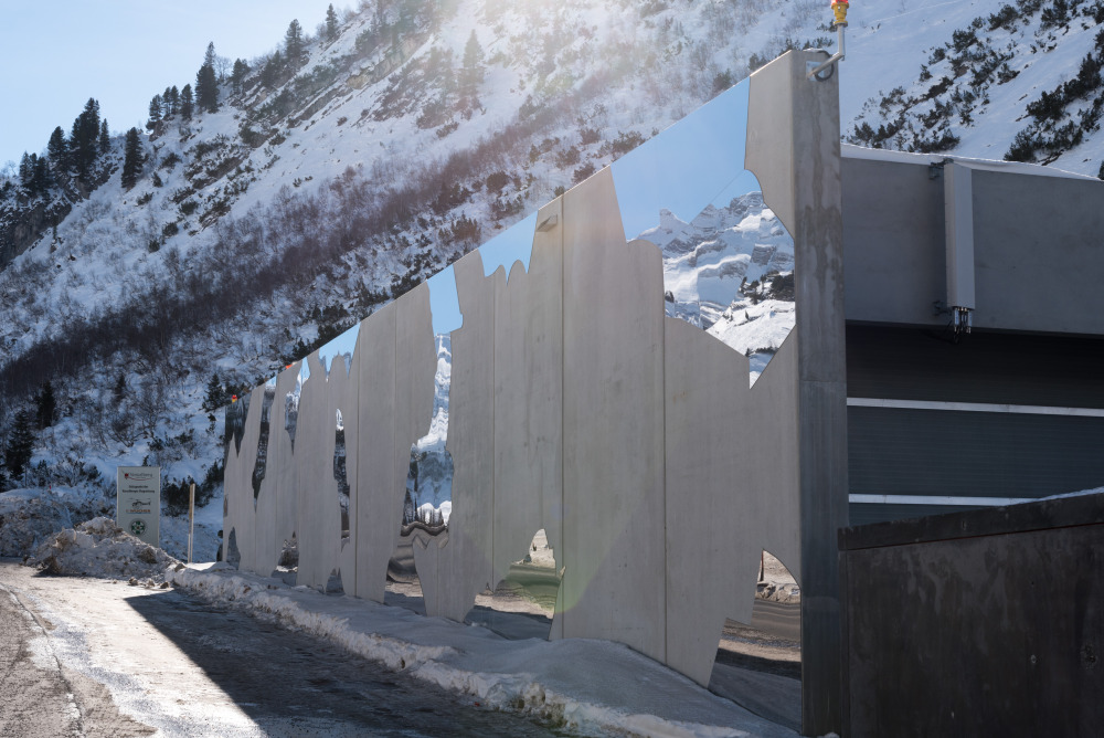 Die Alpen spiegeln sich in den Metallplatten an der Hauswand des Heliport wider